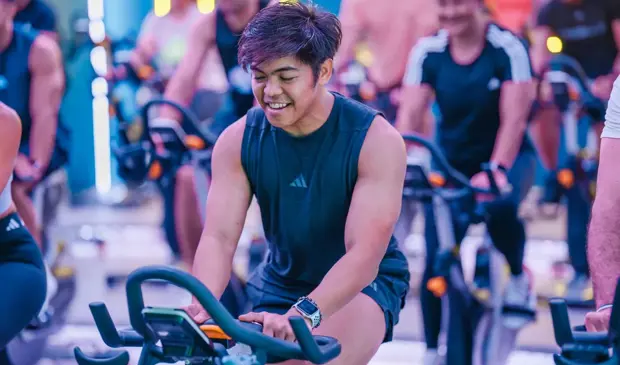 Man focused during a LES MILLS SPRINT class at GymNation, riding an indoor bike in a dynamic group setting.