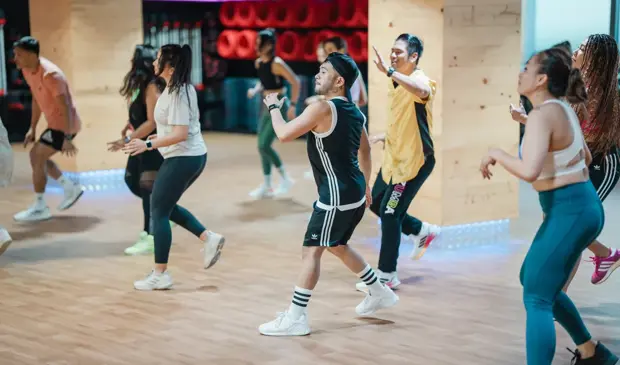 A dynamic group of GymNation members following a high-energy BODYJAM dance routine in a colorful studio, moving together in rhythm and enjoying the music.