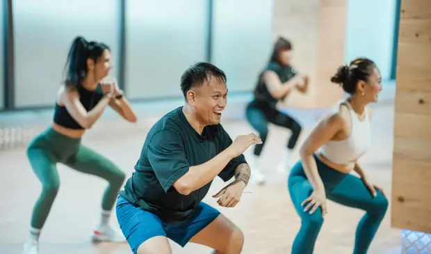 Group of energetic GymNation members enjoying a high-intensity BODYJAM workout in gymnation studio, smiling and dancing together during a cardio dance routine.